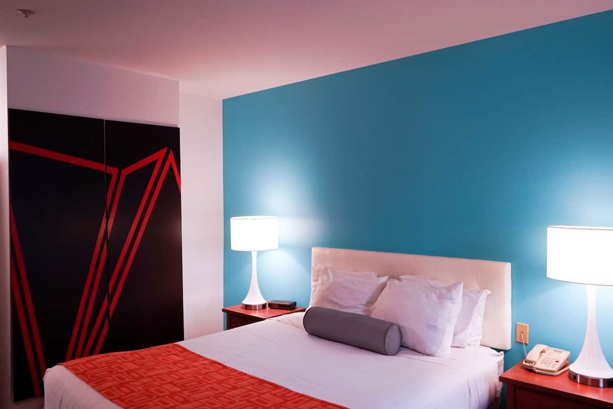 A hotel room with a bed, two bedside tables with lamps, a nightstand with a phone, and a blue accent wall.