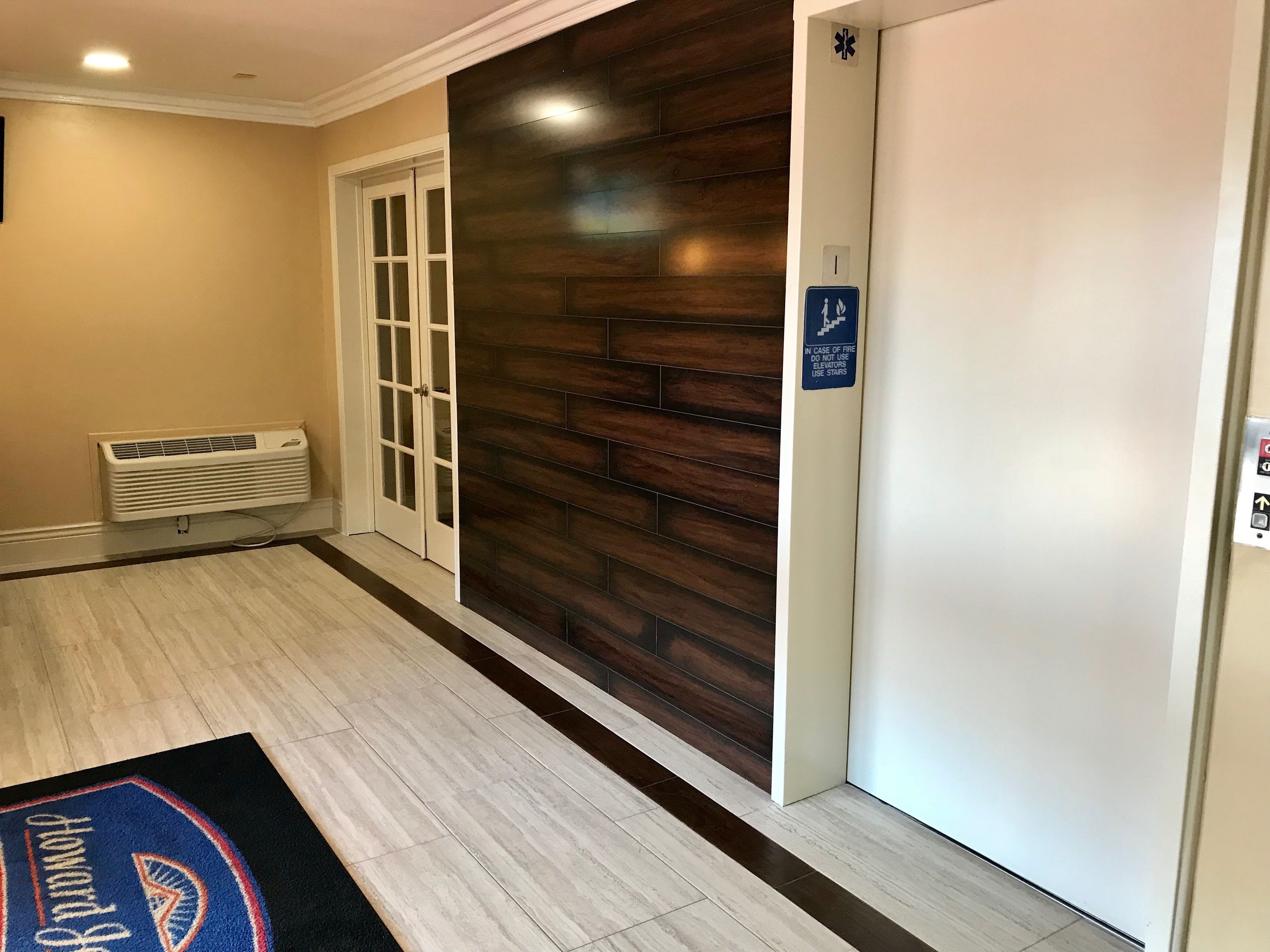 A hallway with a wooden wall, a white door, and a blue emergency exit sign.