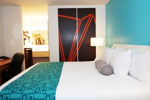 A hotel room with a bed, a desk, a chair, a wardrobe, and a mirror.
