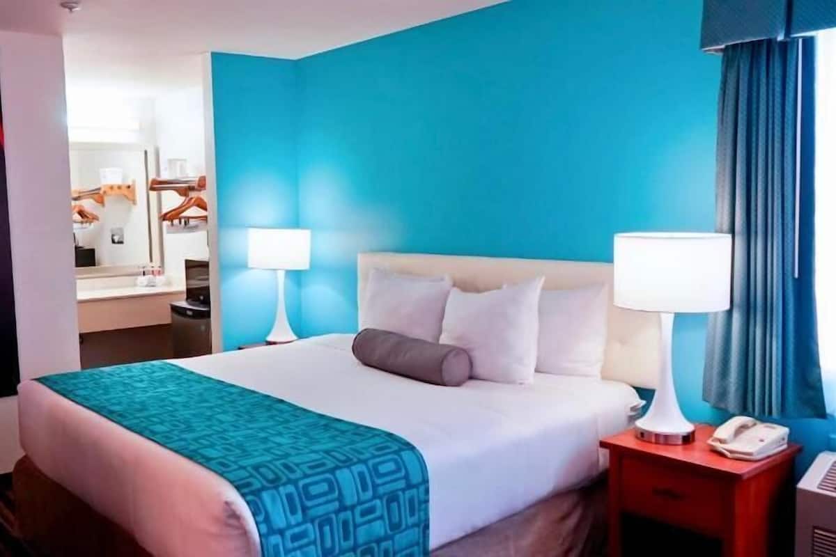 A hotel room with a bed, two bedside tables, a nightstand, a mirror, and a bathroom visible in the background.