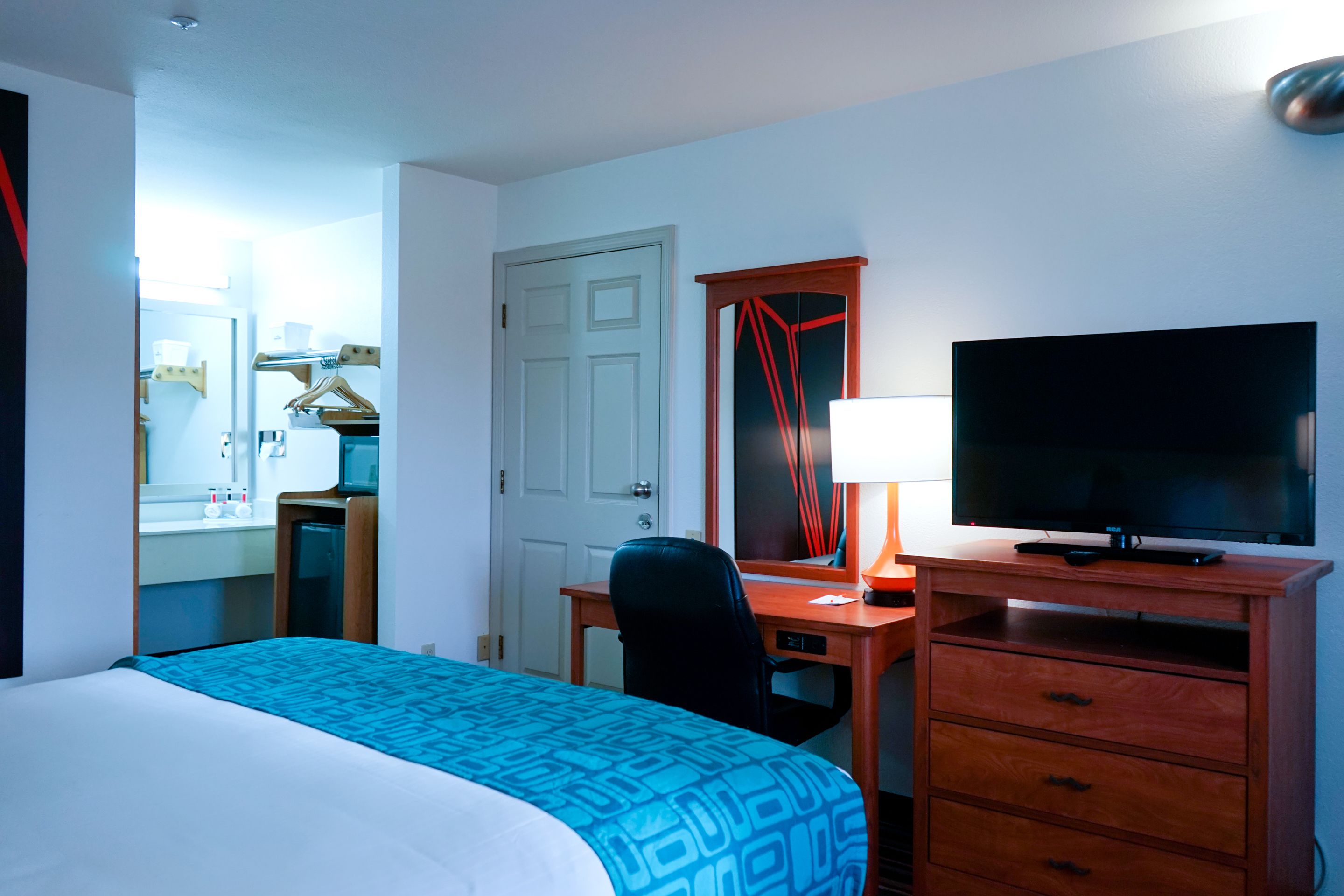 A hotel room with a bed, a desk, a television, a mirror, and a dresser.