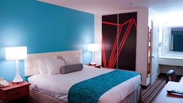 A hotel room with a large bed, two bedside tables with lamps, a desk with a chair, and a window with curtains.