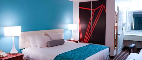 A hotel room with a large bed, two bedside tables with lamps, a desk with a chair, and a window with curtains.