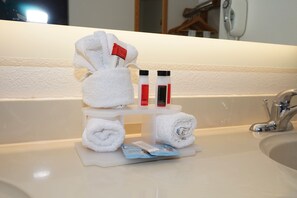 A bathroom sink with a towel rack holding three towels, two bottles of lotion, and a magazine. - Howard Johnson by Wyndham Salinas (Salinas)