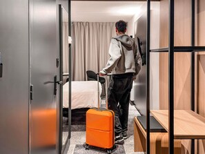 Hotellihuone, jossa on sänky, matkalaukku, työpöytä ja tuoli.