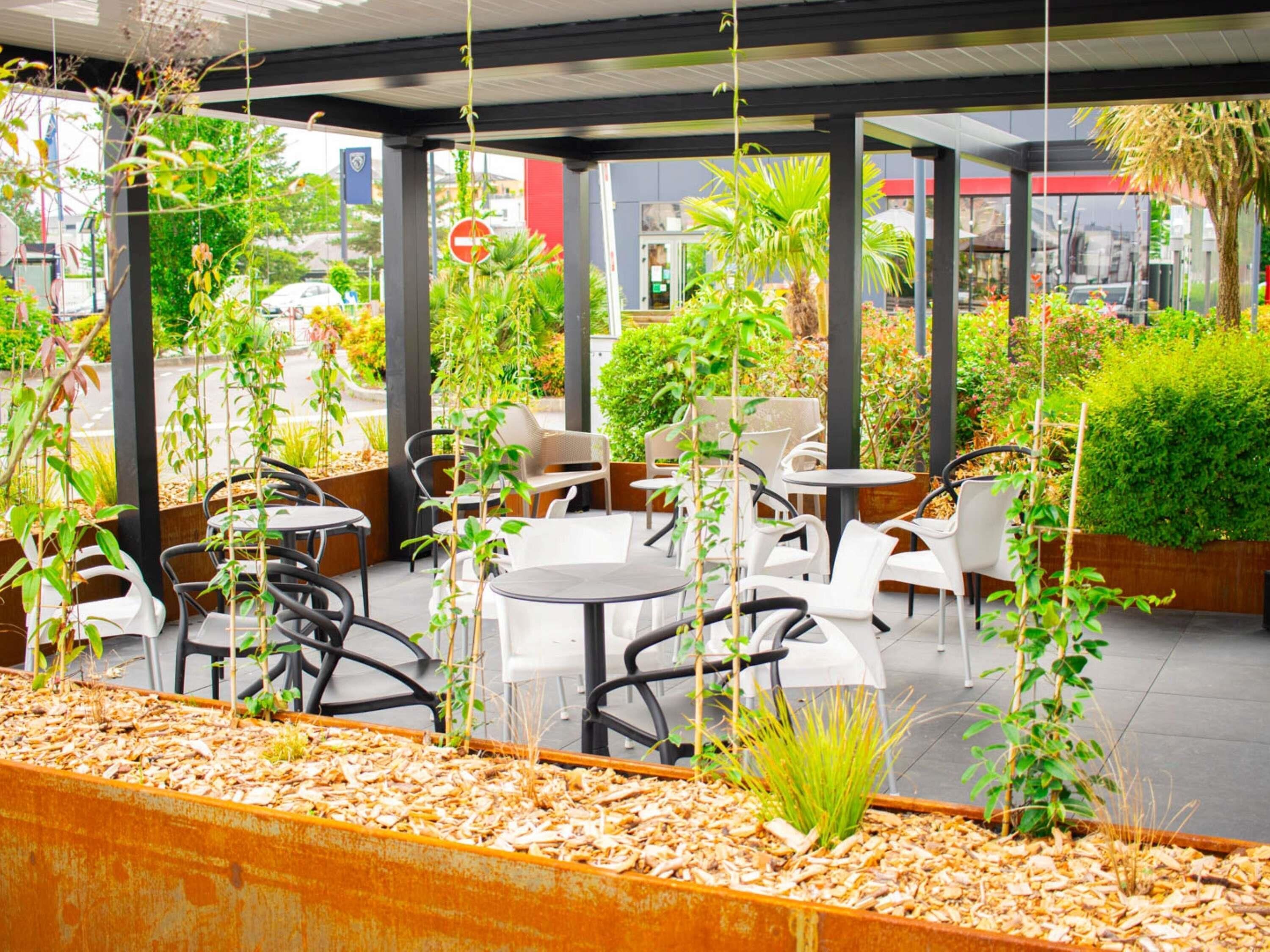An outdoor cafe with tables and chairs, surrounded by greenery and plants.