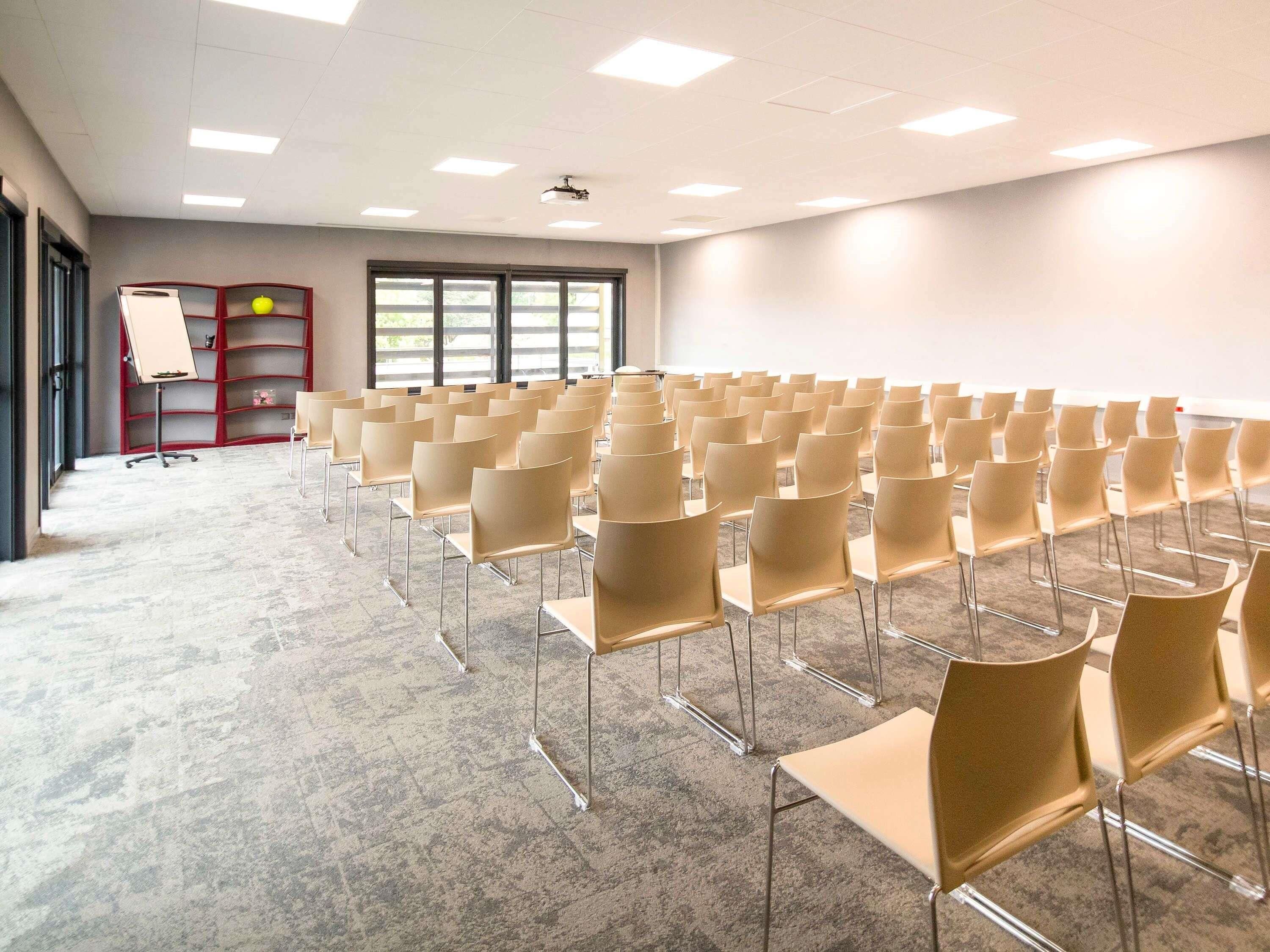 A conference room with rows of chairs, a whiteboard, and a projector on the ceiling.