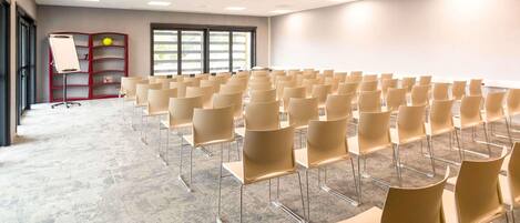 A conference room with rows of chairs, a whiteboard, and a projector on the ceiling.