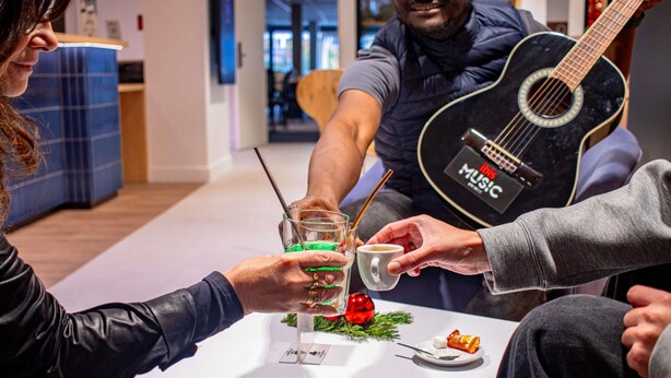 A group of people sitting around a table with a guitar, a glass with a straw, and a plate with food. - ibis Rennes Beaulieu (Cesson-Sevigne)