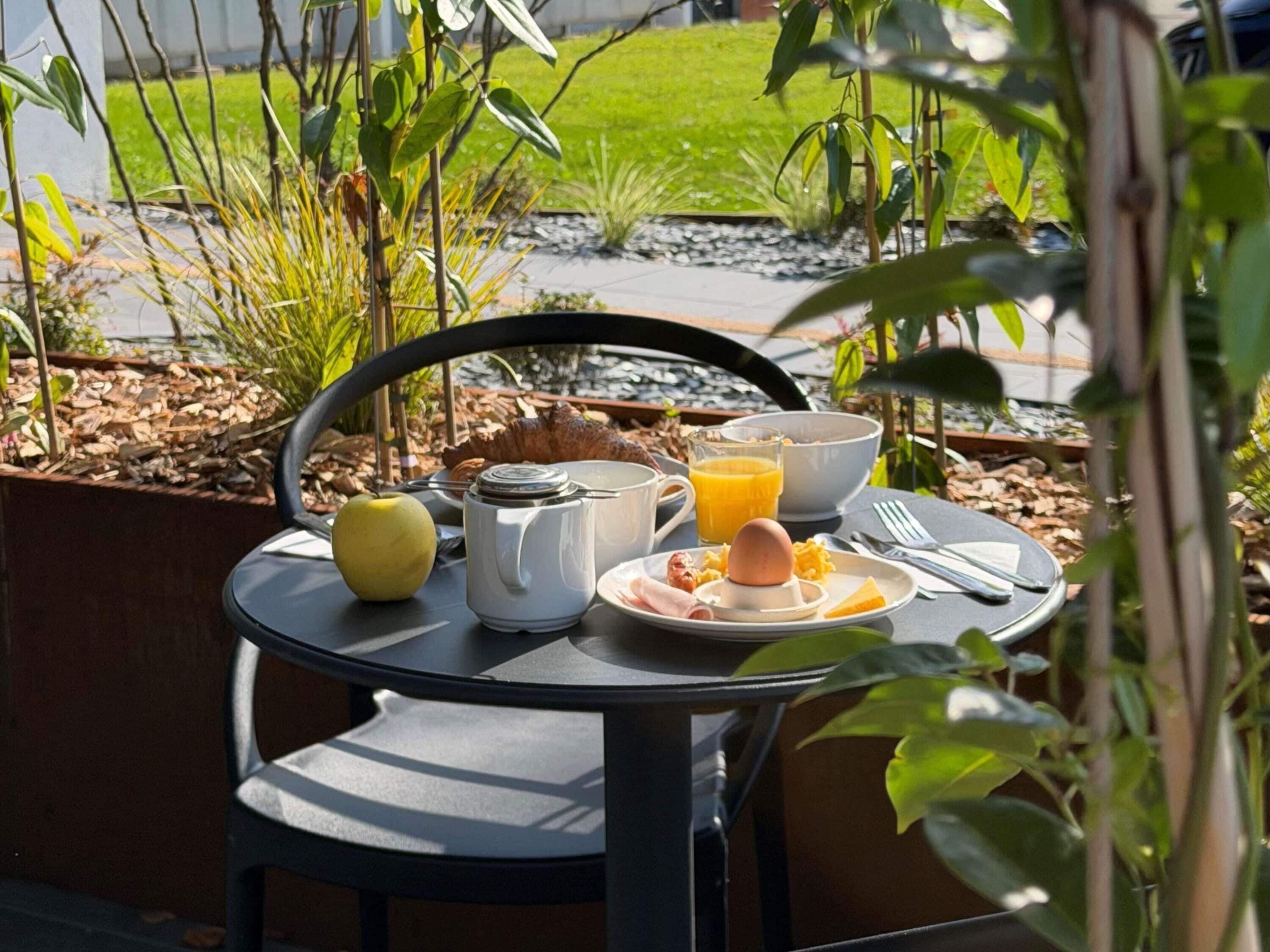 A table set outdoors with breakfast items, a chair, and a view of a garden.