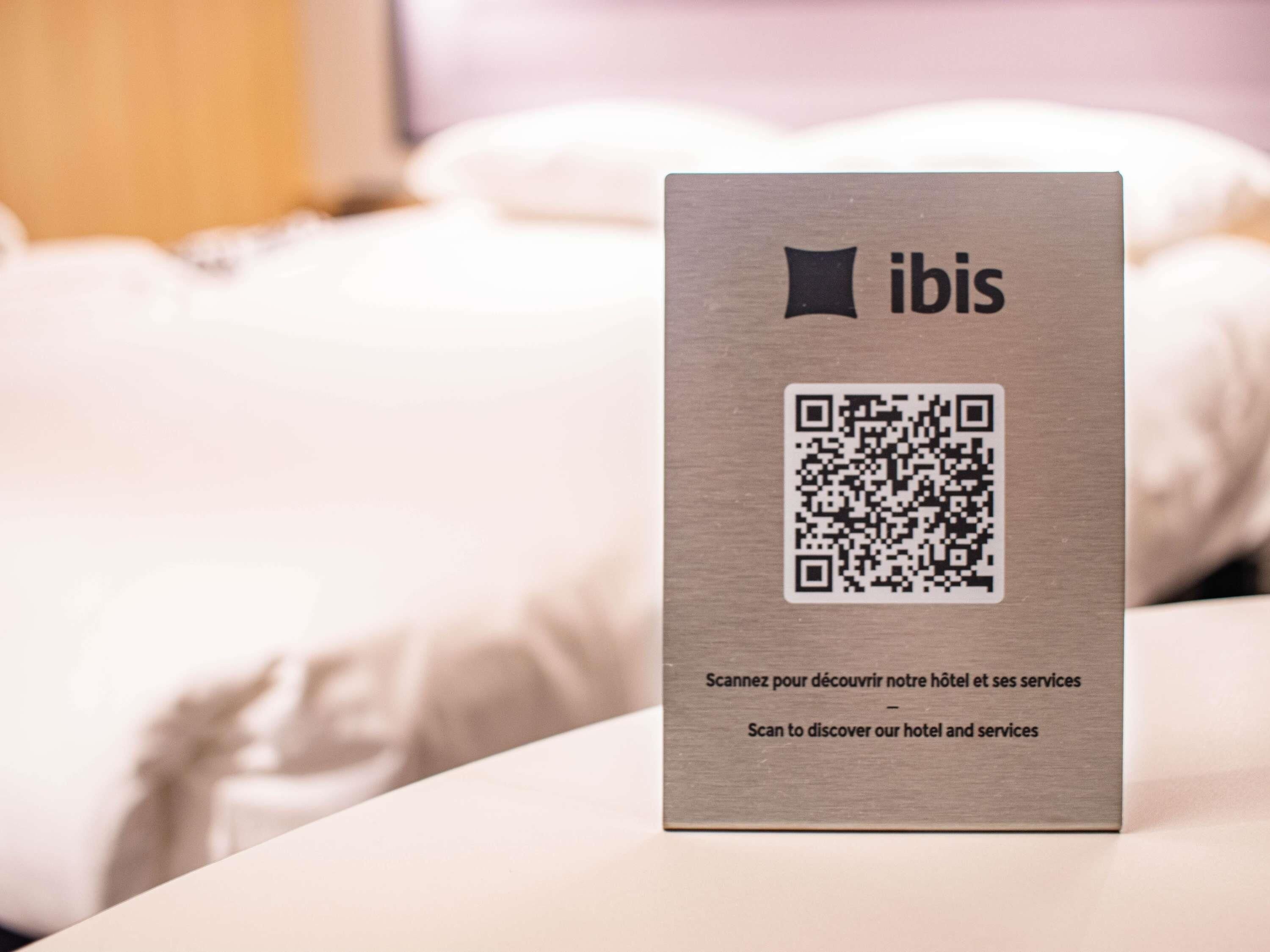 Ein QR-Code auf einem Schild mit dem Schriftzug 'ibis' und Text auf Französisch und Englisch.