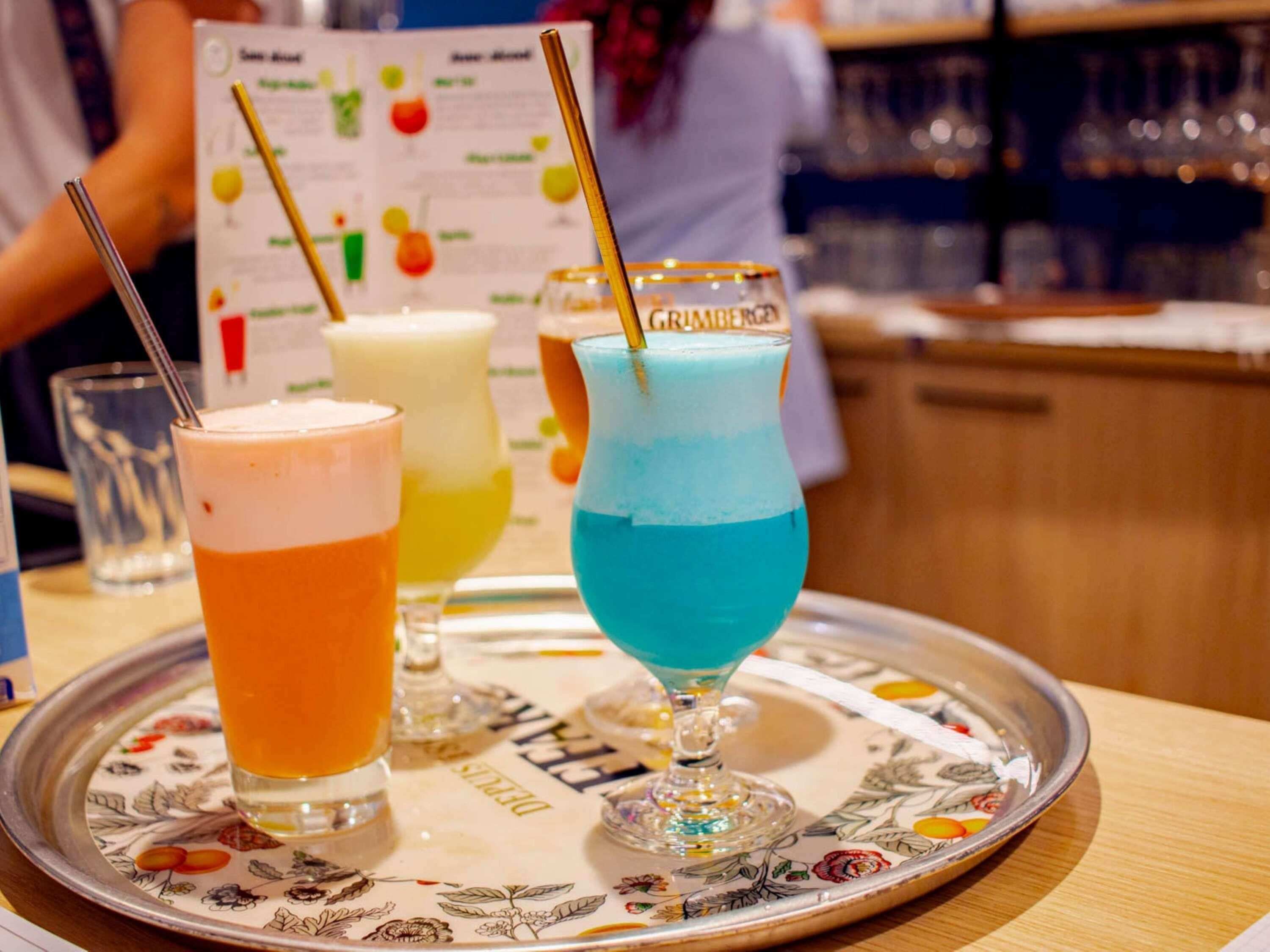 Een dienblad met drie kleurrijke drankjes, een menukaart en een bar op de achtergrond.