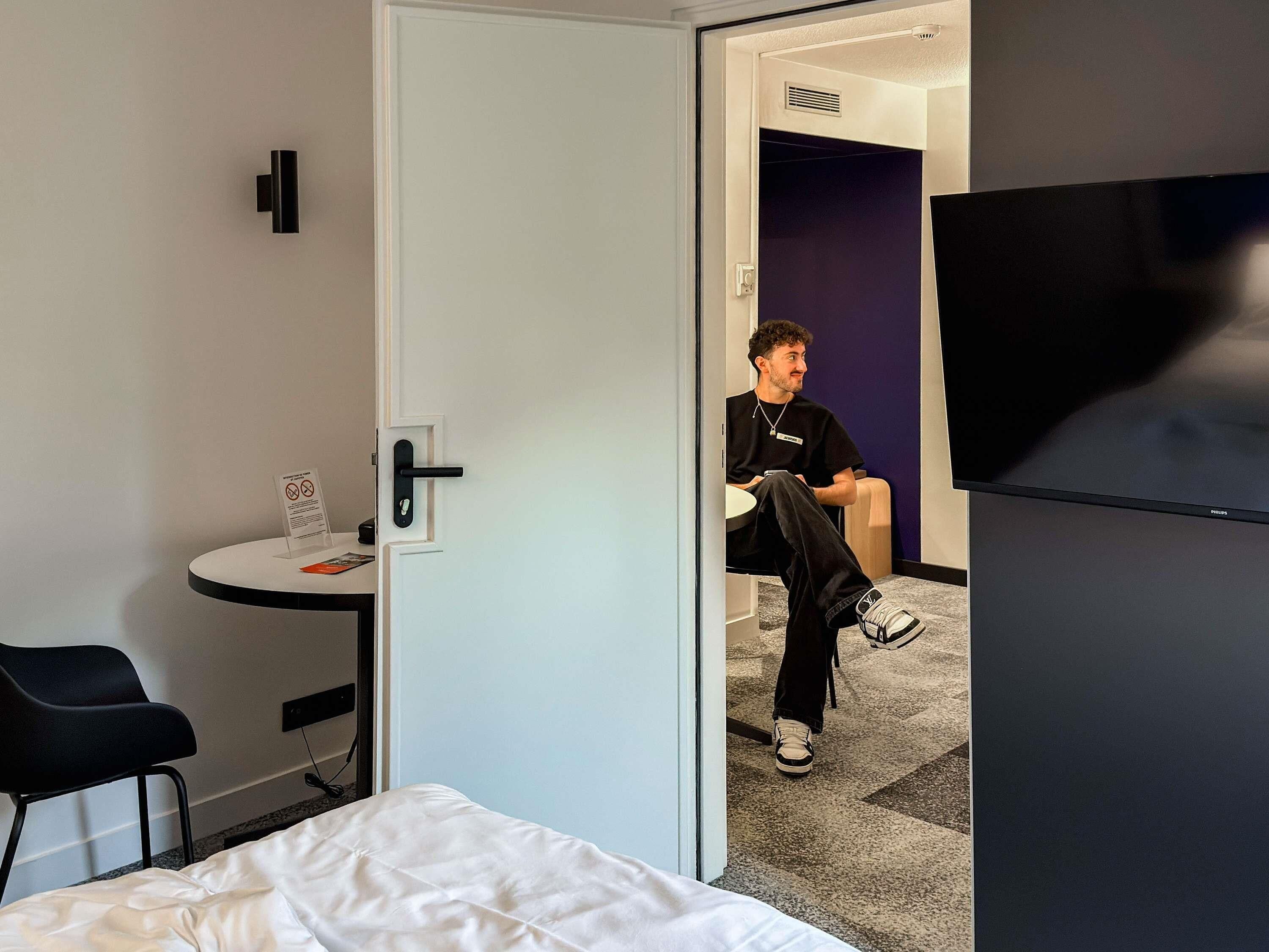 Une chambre d’hôtel équipée d’un lit, d’un bureau, d’une chaise, d’une télévision et d’une porte donnant sur une autre pièce.