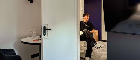 Une chambre d’hôtel équipée d’un lit, d’un bureau, d’une chaise, d’une télévision et d’une porte donnant sur une autre pièce.