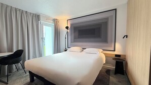 A hotel room with a large bed, a desk, a chair, and a large window with curtains. - ibis Rennes Beaulieu (Cesson-Sevigne)