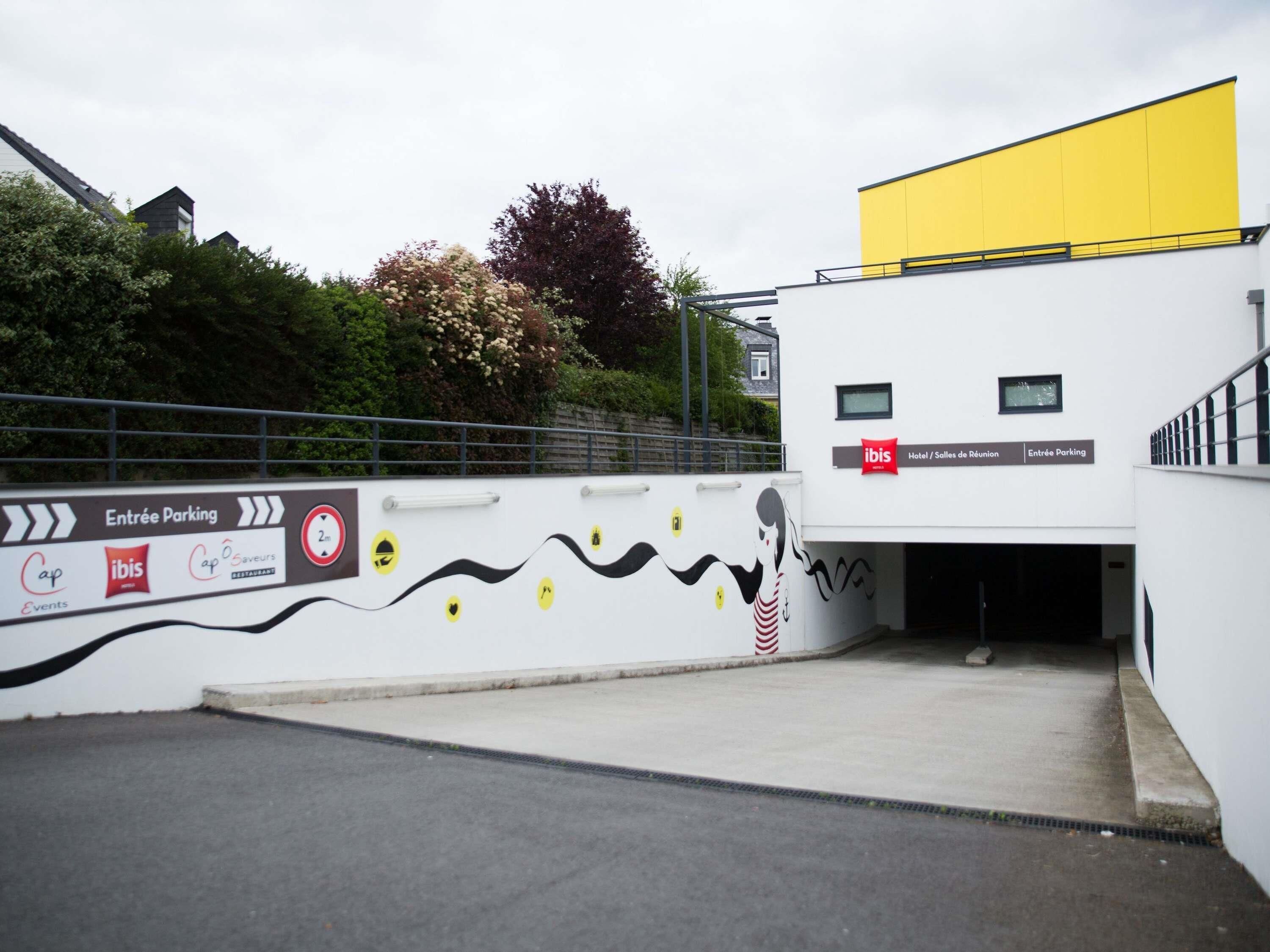 L’entrée d’un hôtel, avec une enseigne indiquant « Hôtel ibis / Salle de réunion » et « Entrée du parking ».
