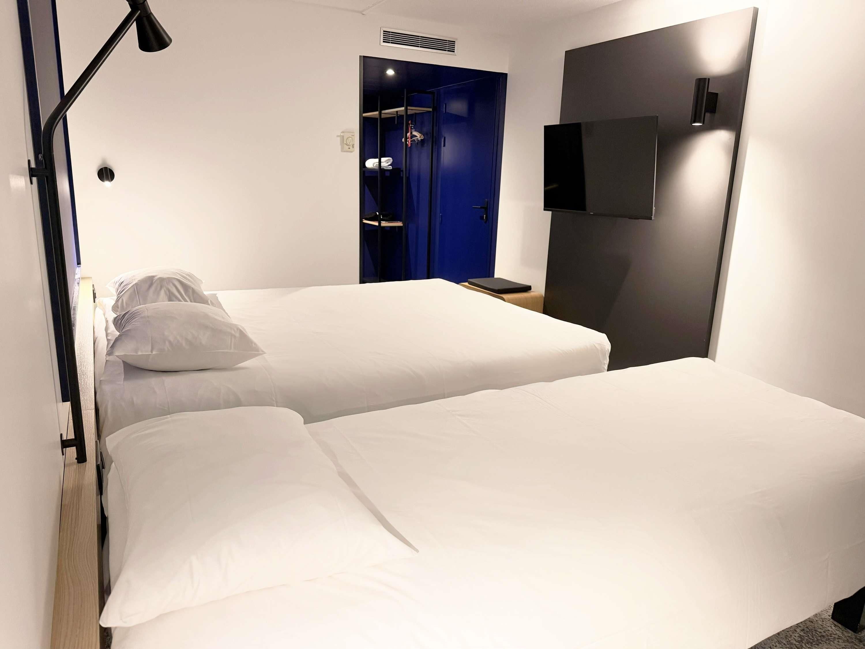 Habitación de hotel con dos camas, una puerta azul, un televisor de pantalla plana y una mesita de noche.