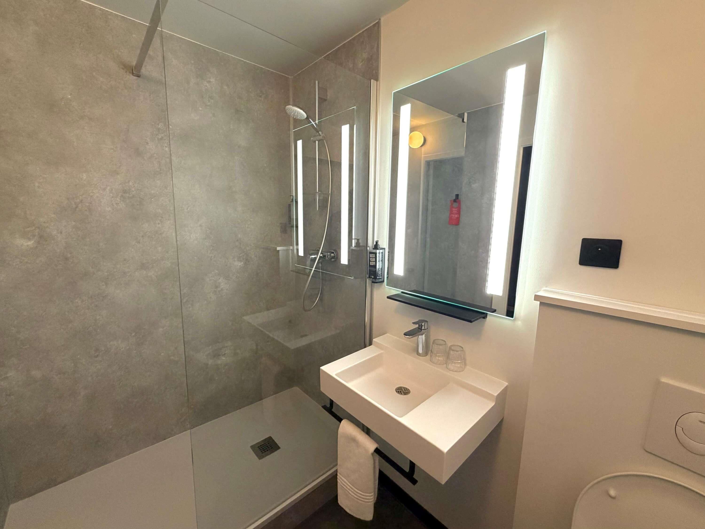 A modern bathroom with a glass-enclosed shower, a white sink, and a mirror with integrated lighting.