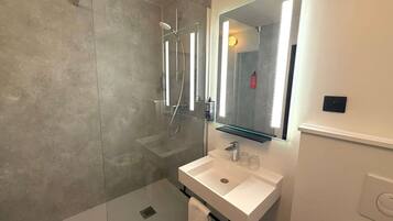 A modern bathroom with a glass-enclosed shower, a white sink, and a mirror with integrated lighting.