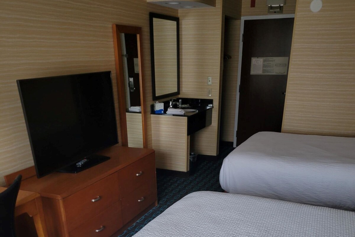 A hotel room with a bed, a TV on a wooden dresser, a mirror, a sink, and a door.