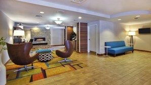 A modern living room with a fireplace, two leather armchairs, a blue sofa, and a patterned rug. - Fairfield Inn By Marriott Ann Arbor (Ann Arbor)