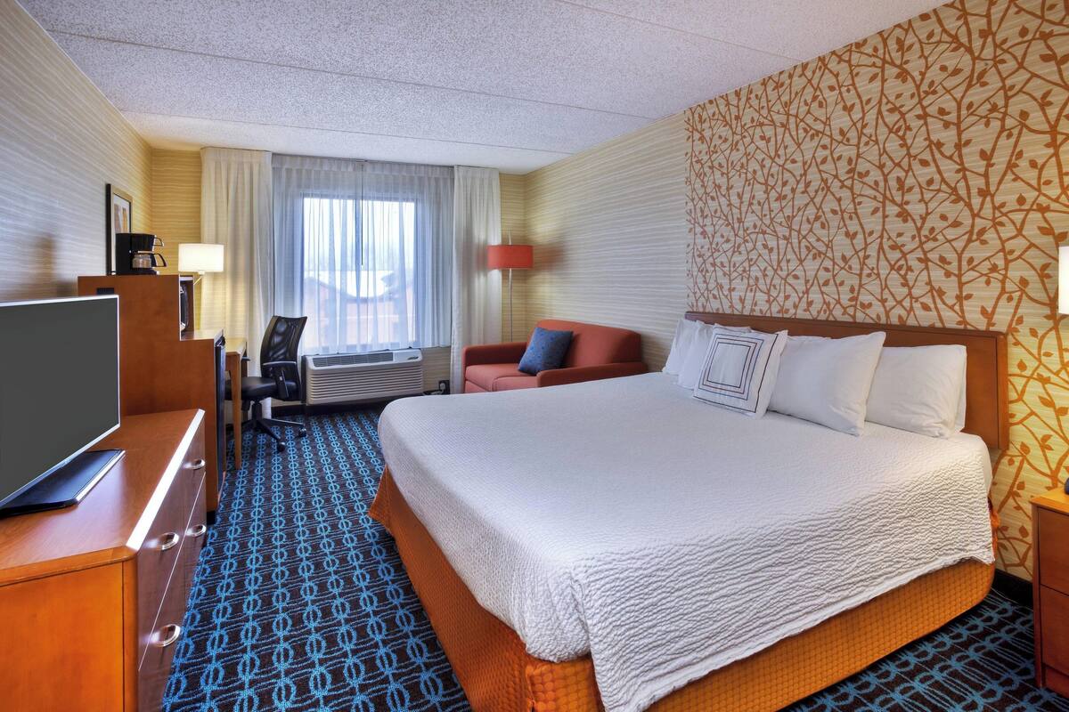 A hotel room with a large bed, a desk with a computer, a TV, and a chair.
