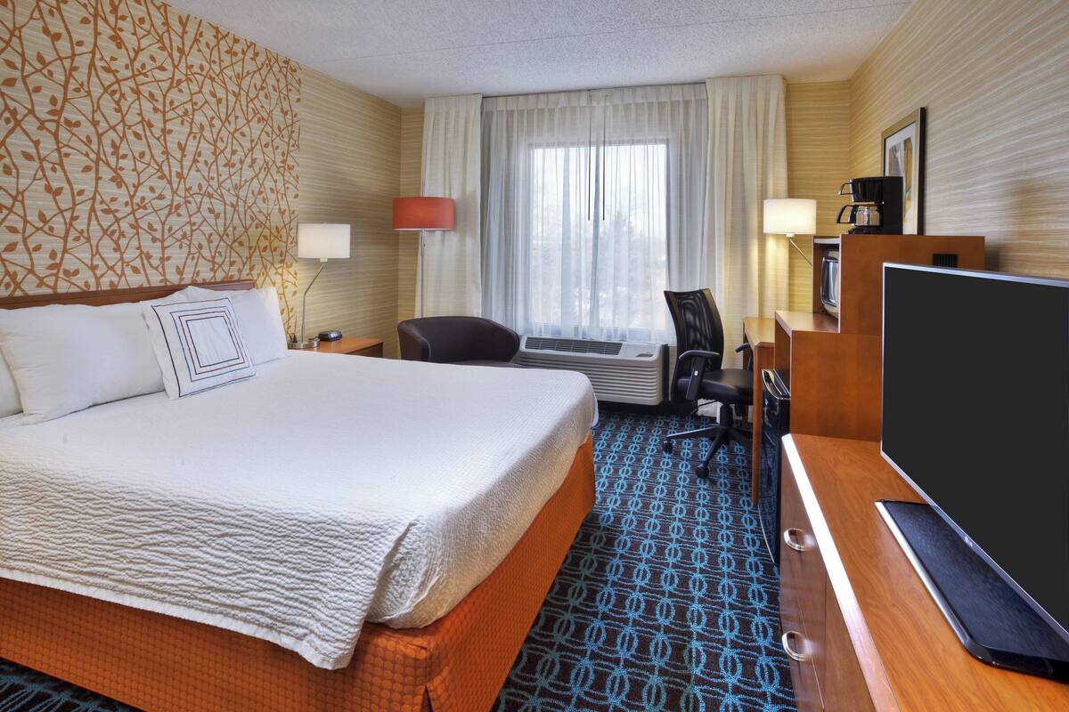 A hotel room with a large bed, a desk with a computer, a TV, and a coffee maker.