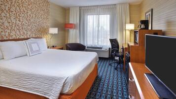 A hotel room with a large bed, a desk with a computer, a TV, and a coffee maker.
