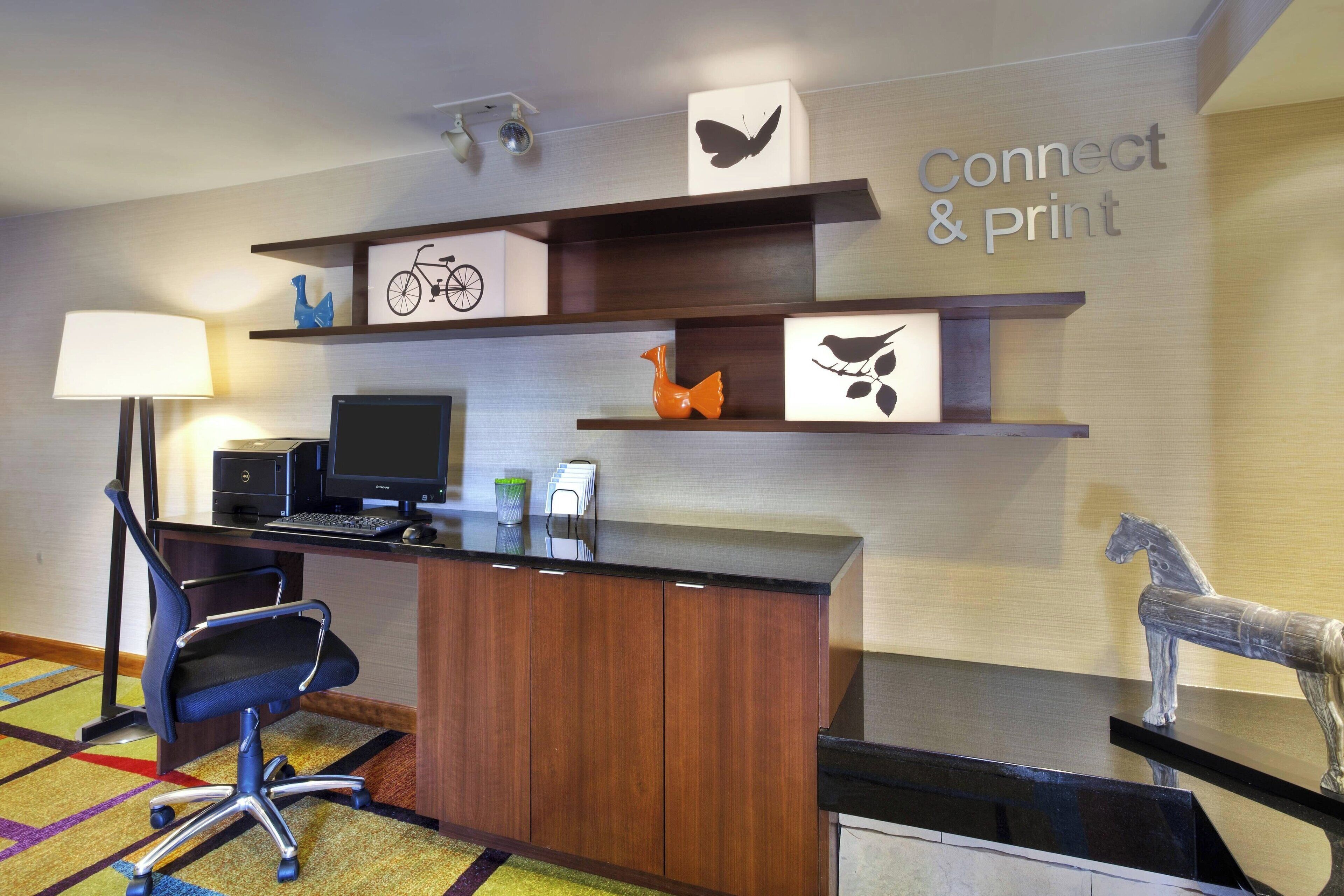 A modern office space with a desk, computer, and office chair. There are shelves with decorative items and a sign that reads "Connect & Print".