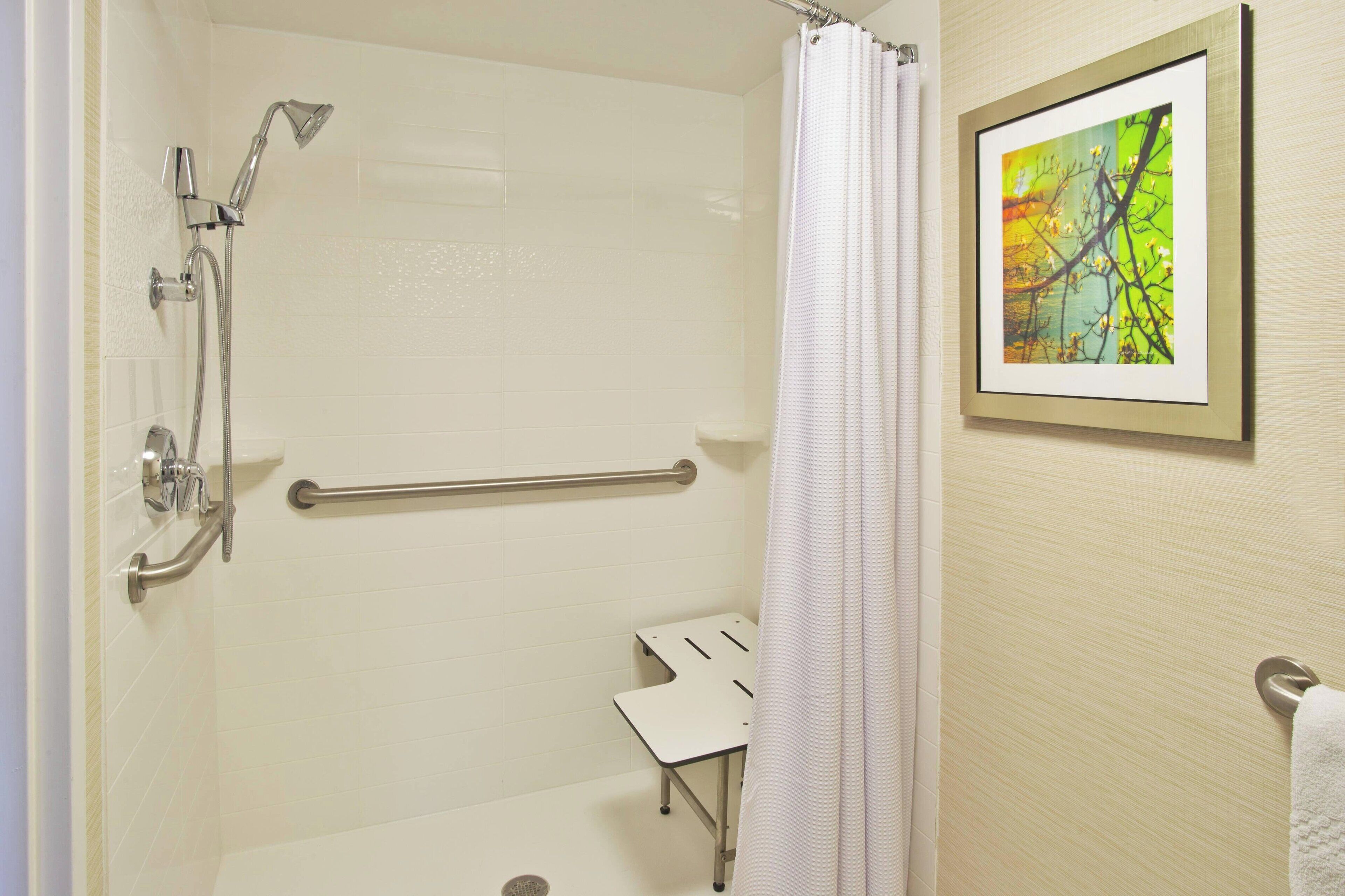 A shower area with a handrail, a showerhead, and a framed picture on the wall.