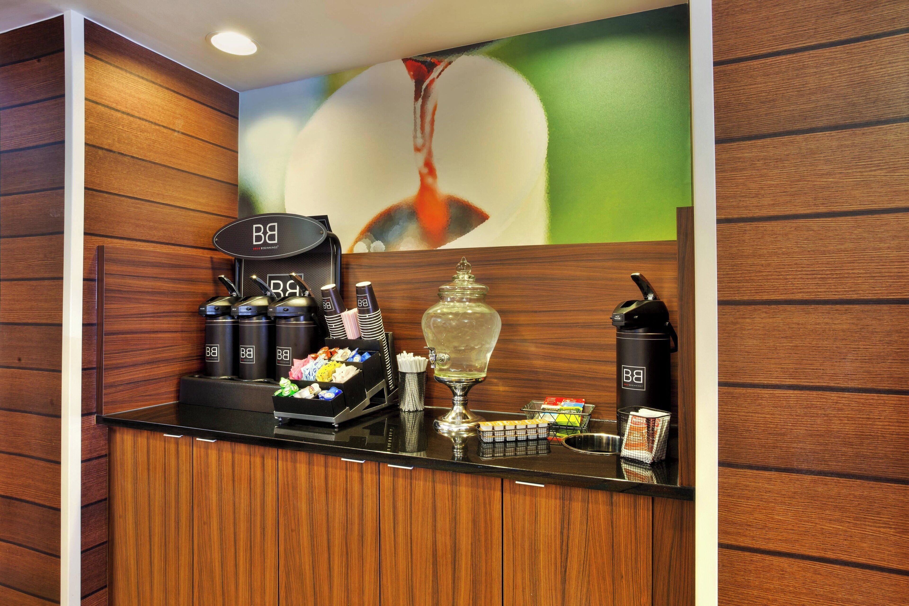 A hotel reception area with a coffee station, tea dispensers, and a decorative vase.
