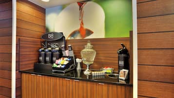 A hotel reception area with a coffee station, tea dispensers, and a decorative vase.