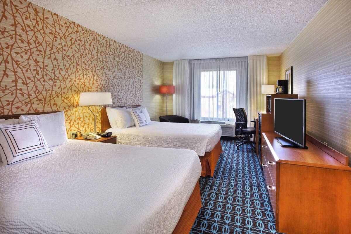 A hotel room with two beds, a desk, a television, and a patterned carpet.