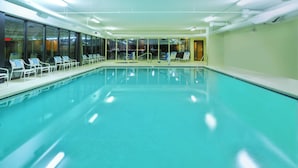 An indoor swimming pool with clear water, surrounded by lounge chairs and a glass wall offering a view of the outside. - Fairfield Inn By Marriott Ann Arbor (Ann Arbor)