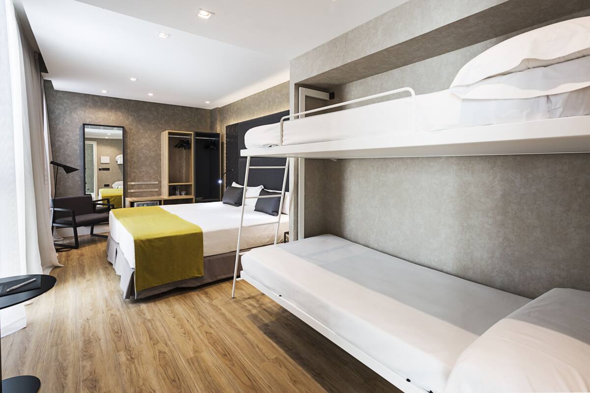 A modern hotel room with a bunk bed, a desk, a chair, a mirror, and a bedside table.