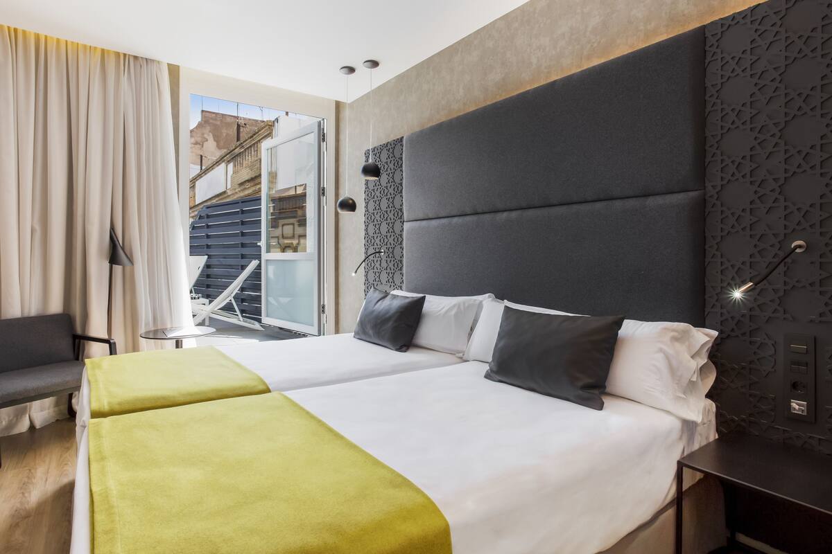 A modern hotel room with a large bed, a sofa, and a view of a building outside.