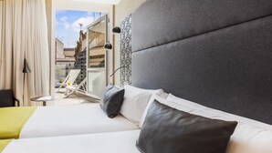 A hotel room with a large bed, a small table, and a view of the outside balcony.