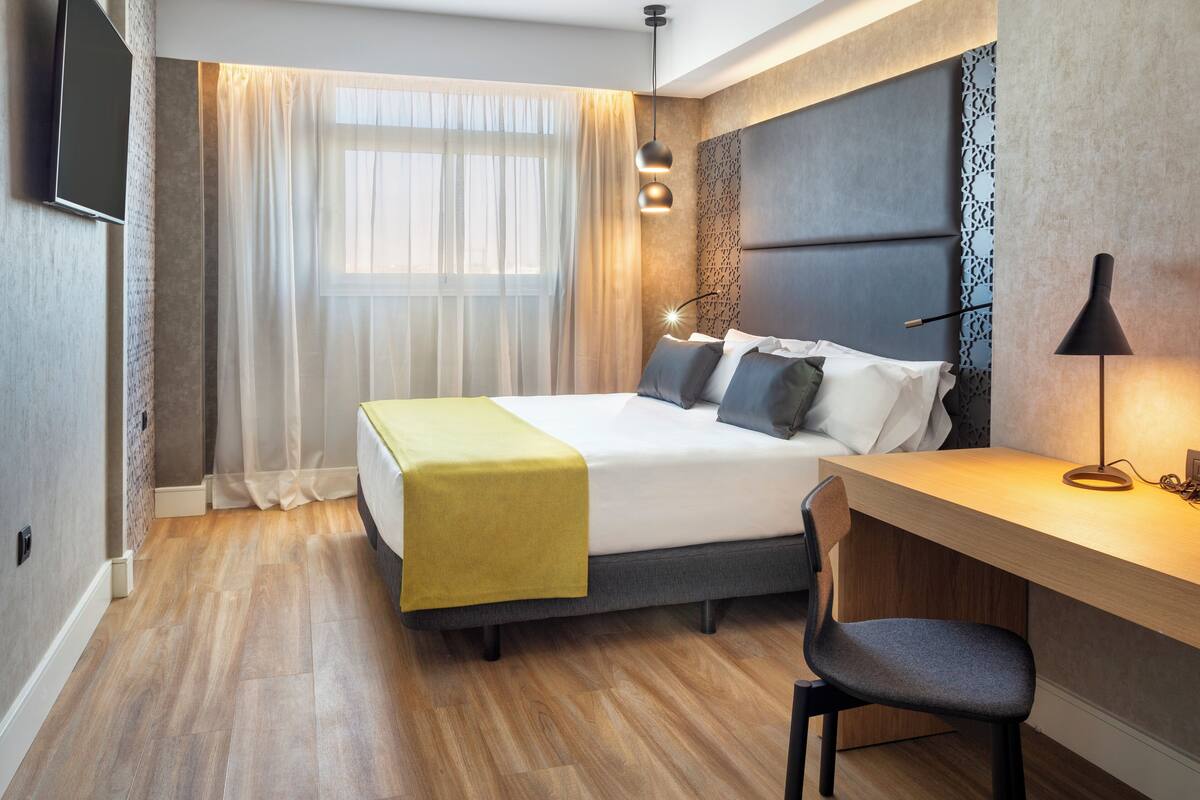 A modern hotel room with a bed, a desk, and a chair.