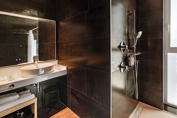 Un baño moderno con un espejo grande, un lavamanos, una ducha con cabezal de ducha manual y un perchero para toallas.