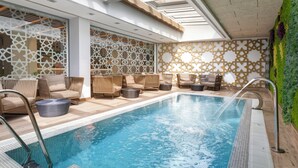 A modern indoor pool area with lounge seating and a decorative wall.