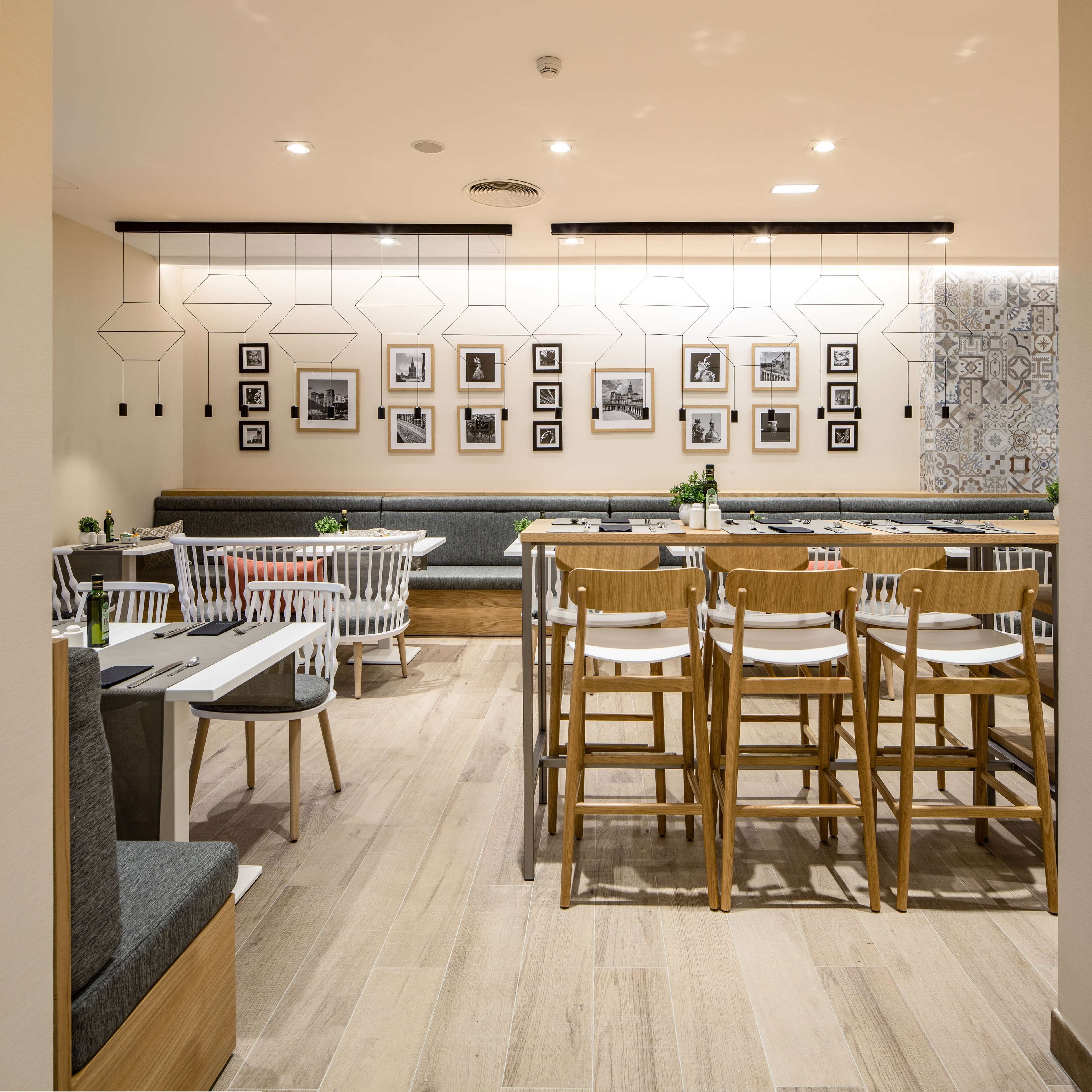 Un comedor moderno con sillas y mesas de madera, arte mural geométrico e iluminación empotrada en el techo.