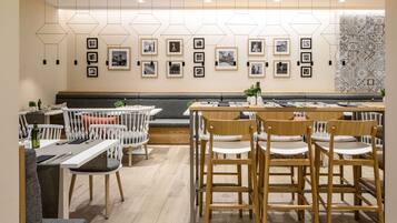 Un comedor moderno con sillas y mesas de madera, arte mural geométrico e iluminación empotrada en el techo.