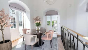 Un comedor con una mesa redonda, dos sillas, un florero con flores y vistas a un edificio a través de amplios ventanales.
