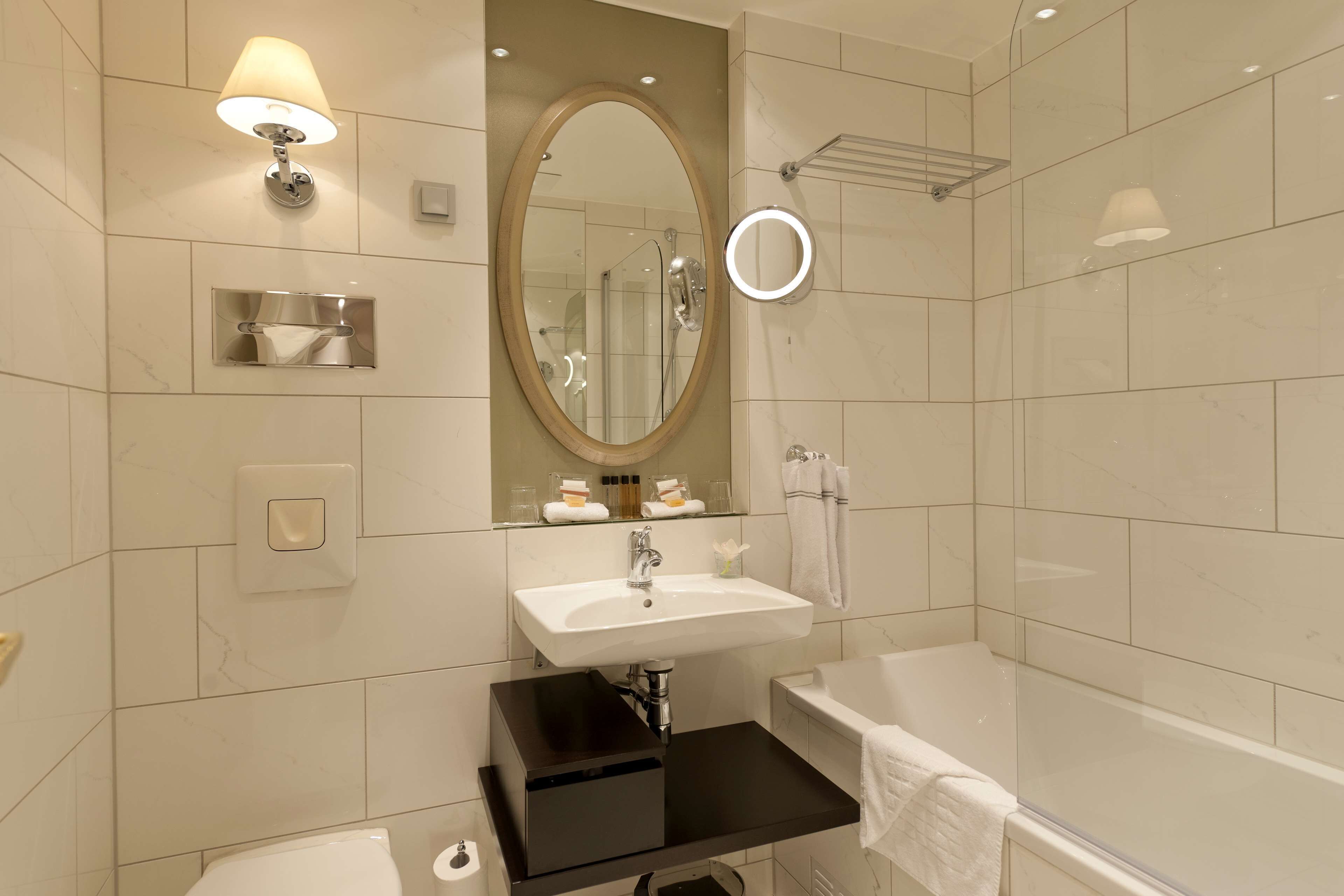 A modern bathroom with a white sink, a mirror, a round vanity mirror, a bathtub, and a towel rack.