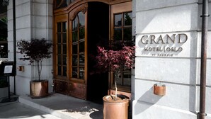 The exterior of the Grand Hotel Oslo with a large wooden entrance, a signboard, and potted plants.