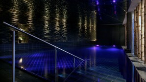 A modern indoor pool area with a glass barrier, stone wall, and ambient lighting.