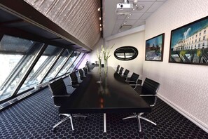 A conference room with a long table, black chairs, a projector, and large windows with a city view.