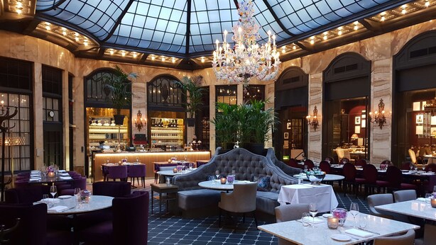 A luxurious dining area with a high ceiling, chandeliers, and a central seating area.