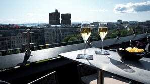 A table with two glasses of white wine and a bowl of chips on a rooftop terrace with a city view.
