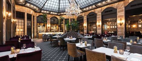 Un restaurante espacioso con techo alto y cúpula de cristal, con un mobiliario elegante e iluminación ambiental.